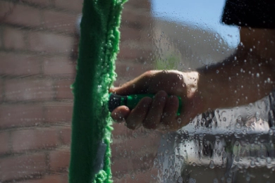 Ein Fensterputzer reinigt ein Schaufenster mit einem Wischer und Schaum.